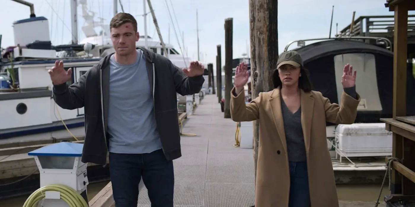 Peter and Rose with their hands up in a dockyard in The Night Agent Image