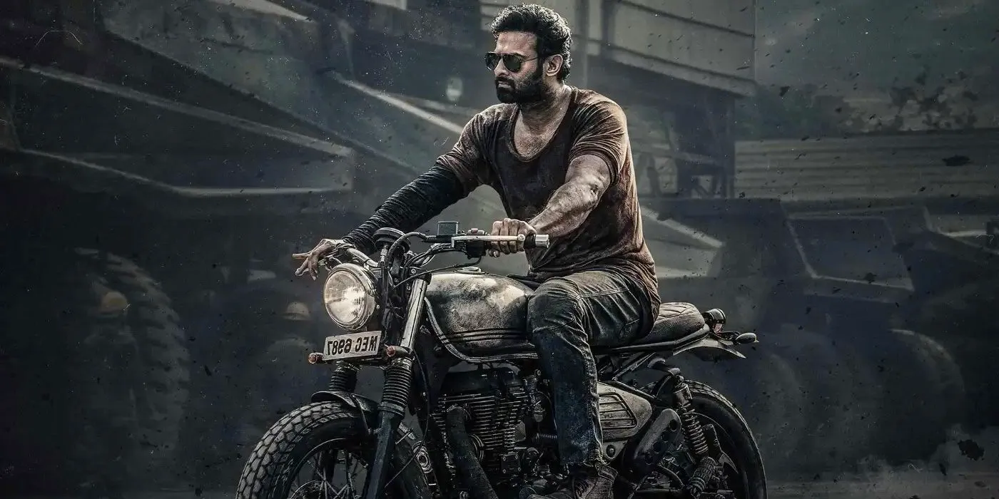 Prabhas as Salaar riding a motorcycle through a construction yard in Salaar Part 1 Ceasefire. Image