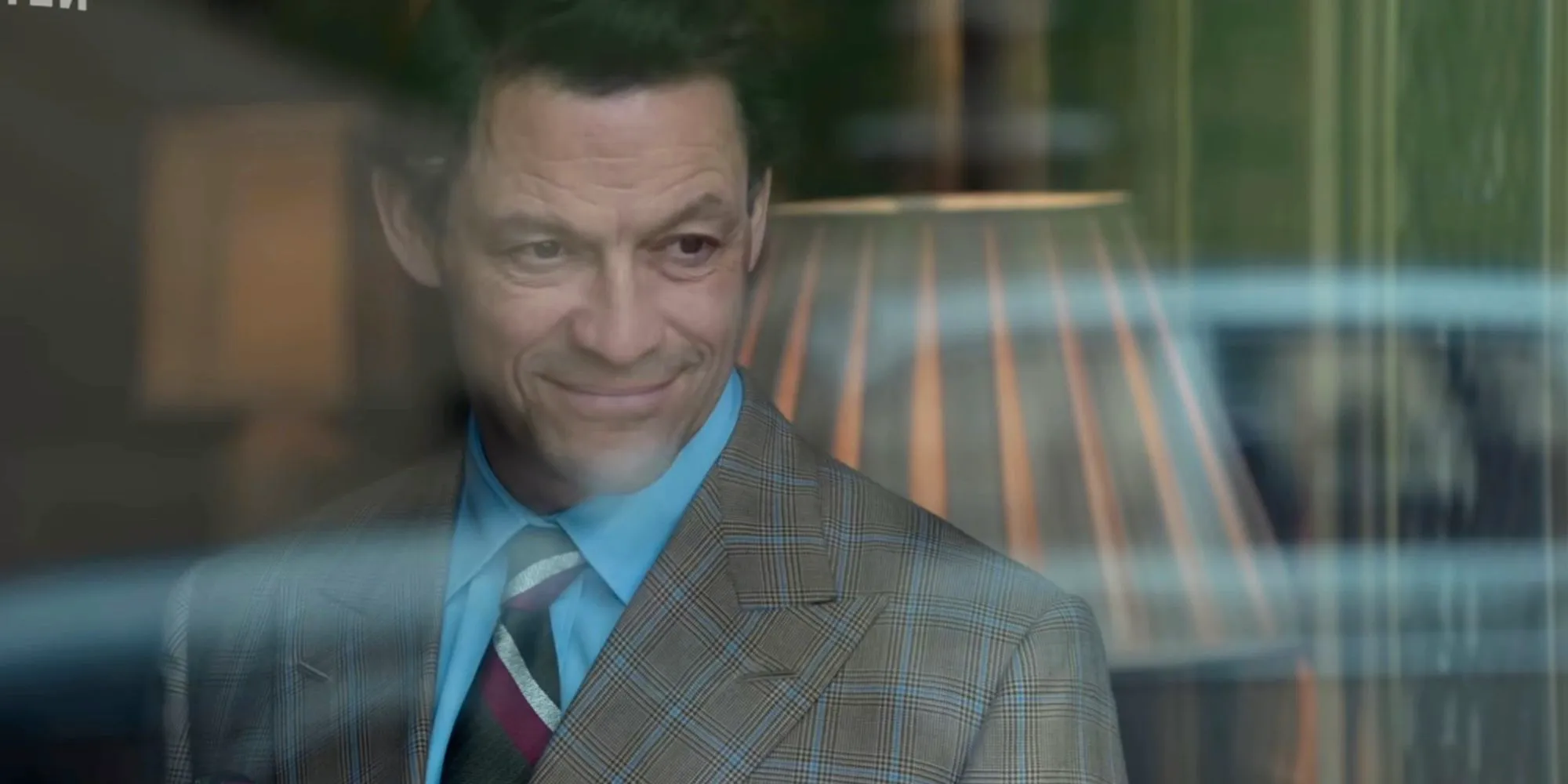 Prince Charles (Dominic West) smiles while looking out the window in The Crown. Image