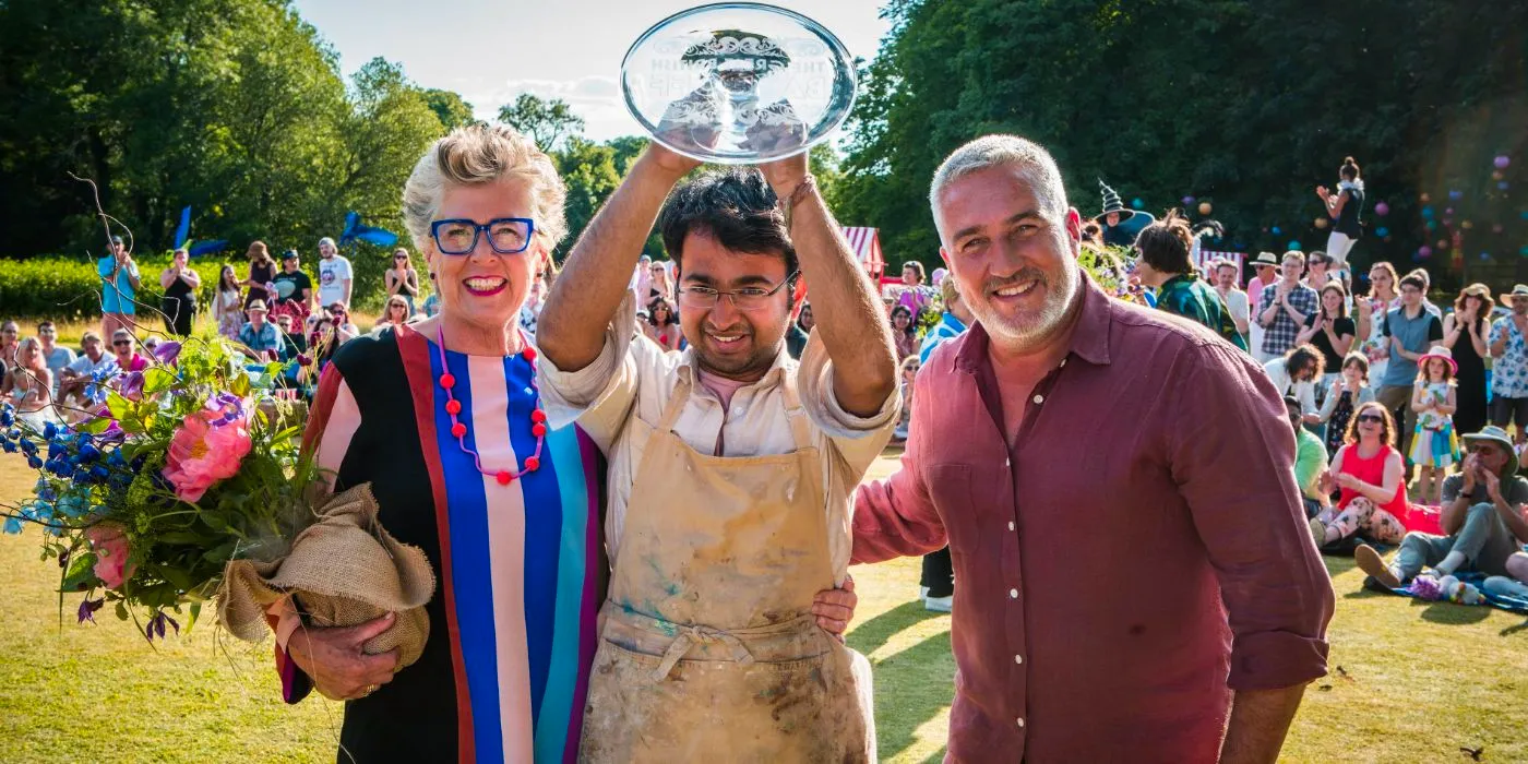 Rahul Mandal holding his trophy alongside Prue and Paul in The Great British Bake Off. Image