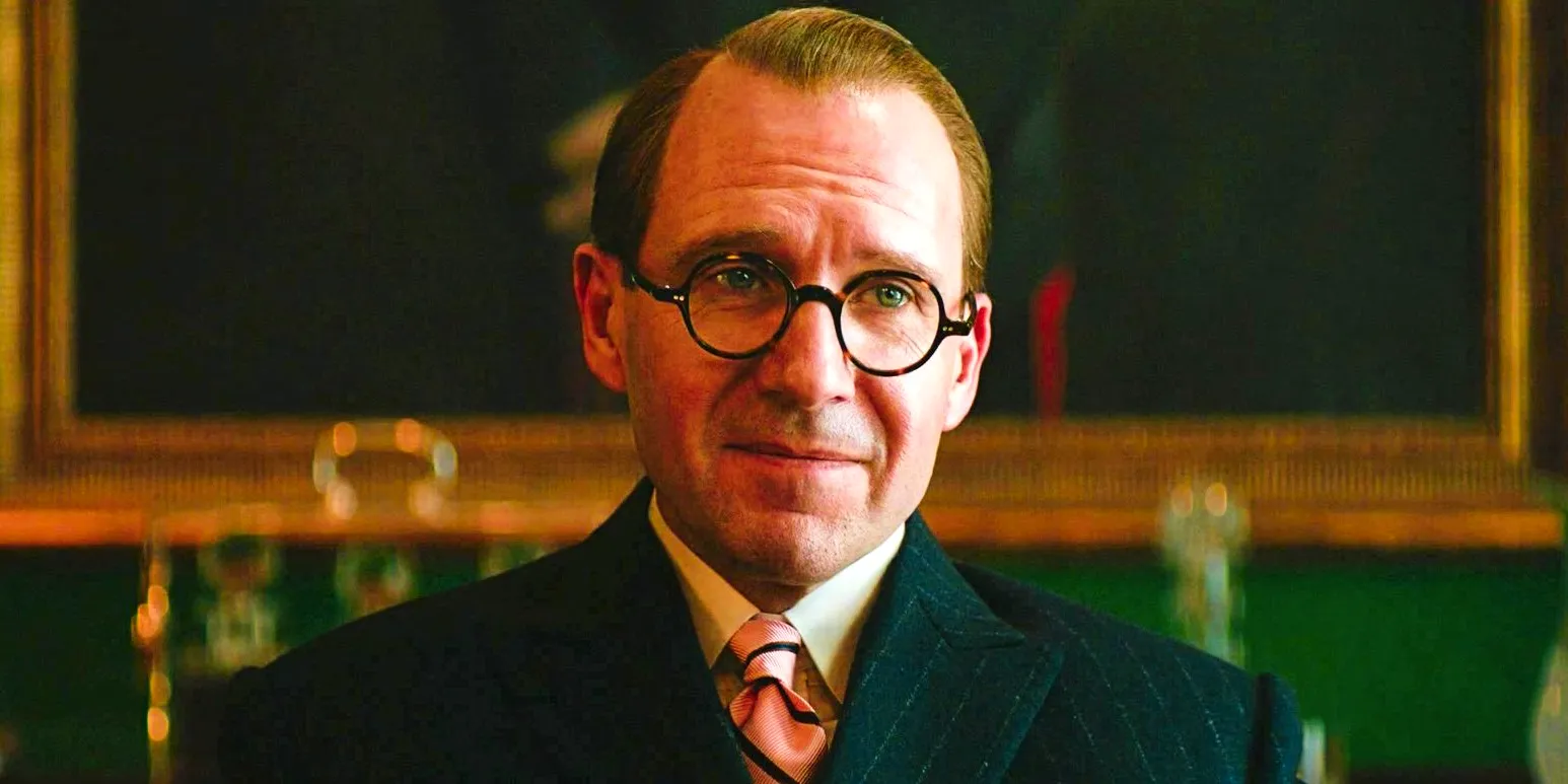 Ralph Fiennes wearing glasses and softly smiling in The King's Man. Image