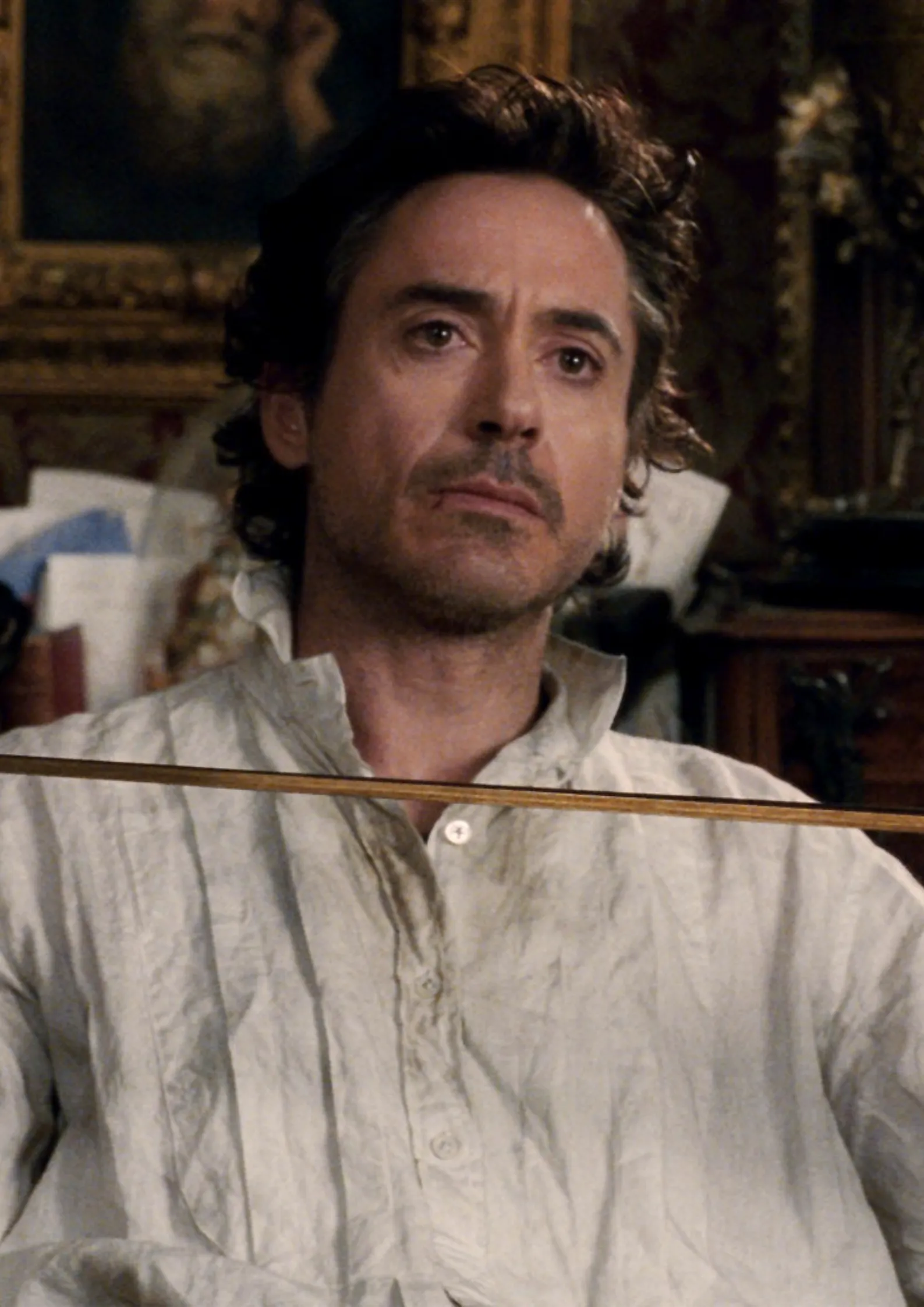 Robert Downey Jr. as Sherlock Holmes in Sherlock Holmes (2009) sitting in a chair while holding a violin bow Image