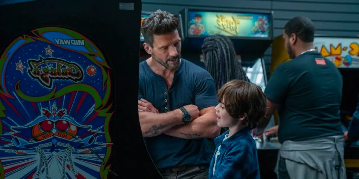 Roy and his son at an arcade, talking as the son plays a game in Boss Level Image