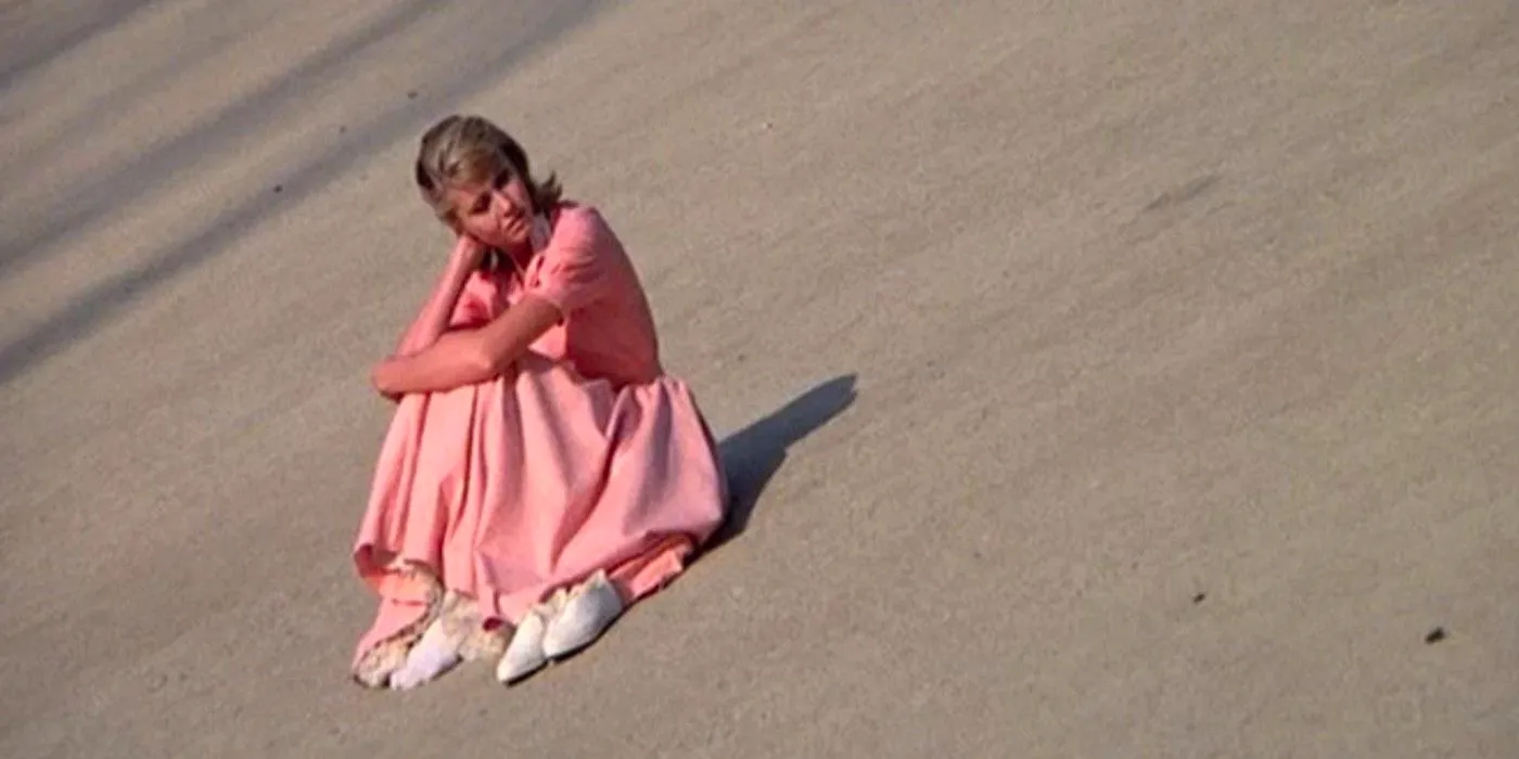 Sandy sitting on the concrete in her pink dress in Grease Image