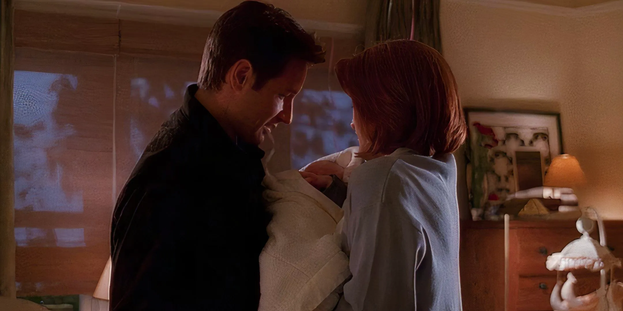 Scully and Mulder holding and smiling at their son, William, in The X-Files. Image