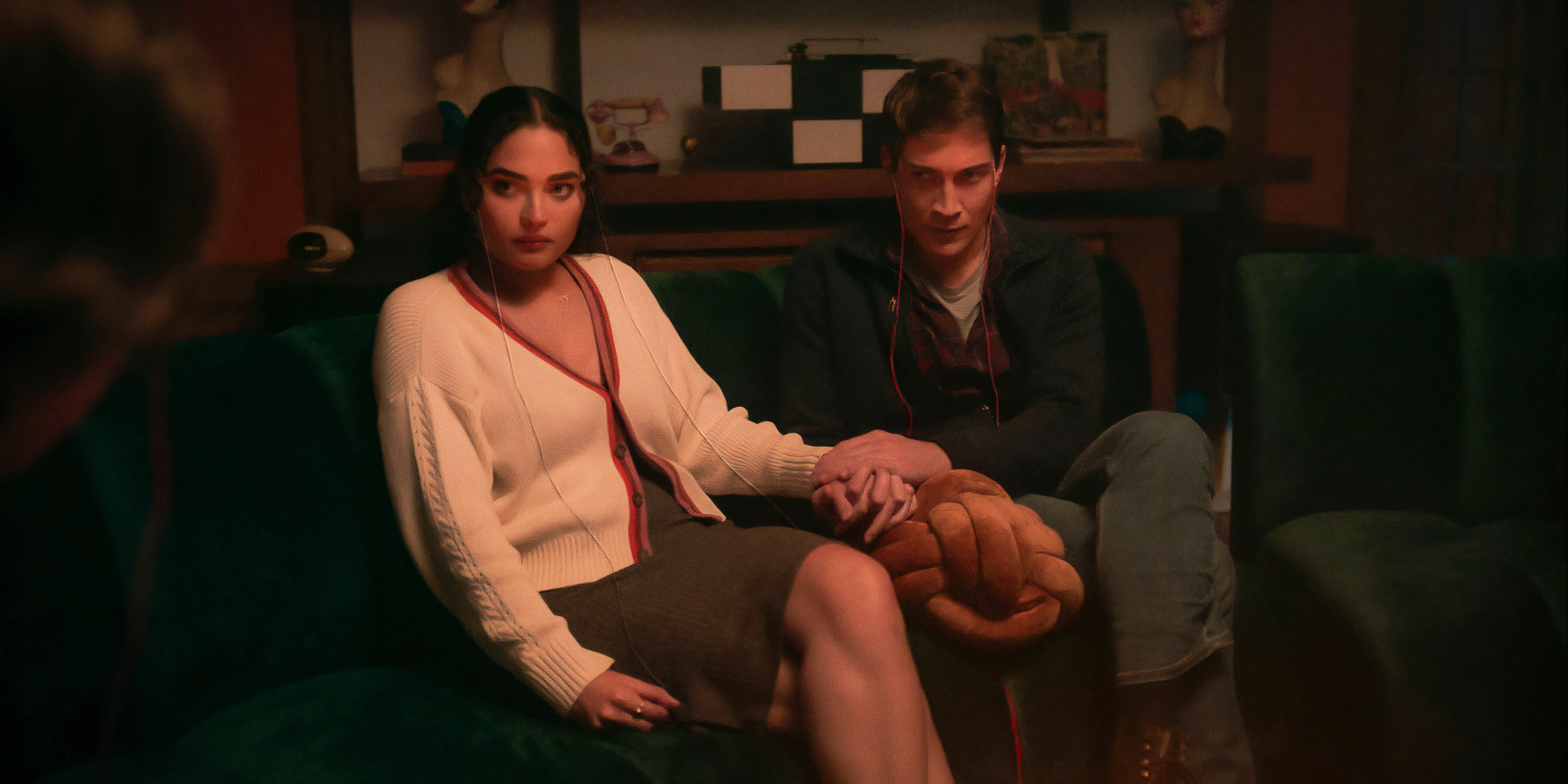 Shelby and Cyrus hold hands while sitting on the couch in Netflix's It's What's Inside. Image