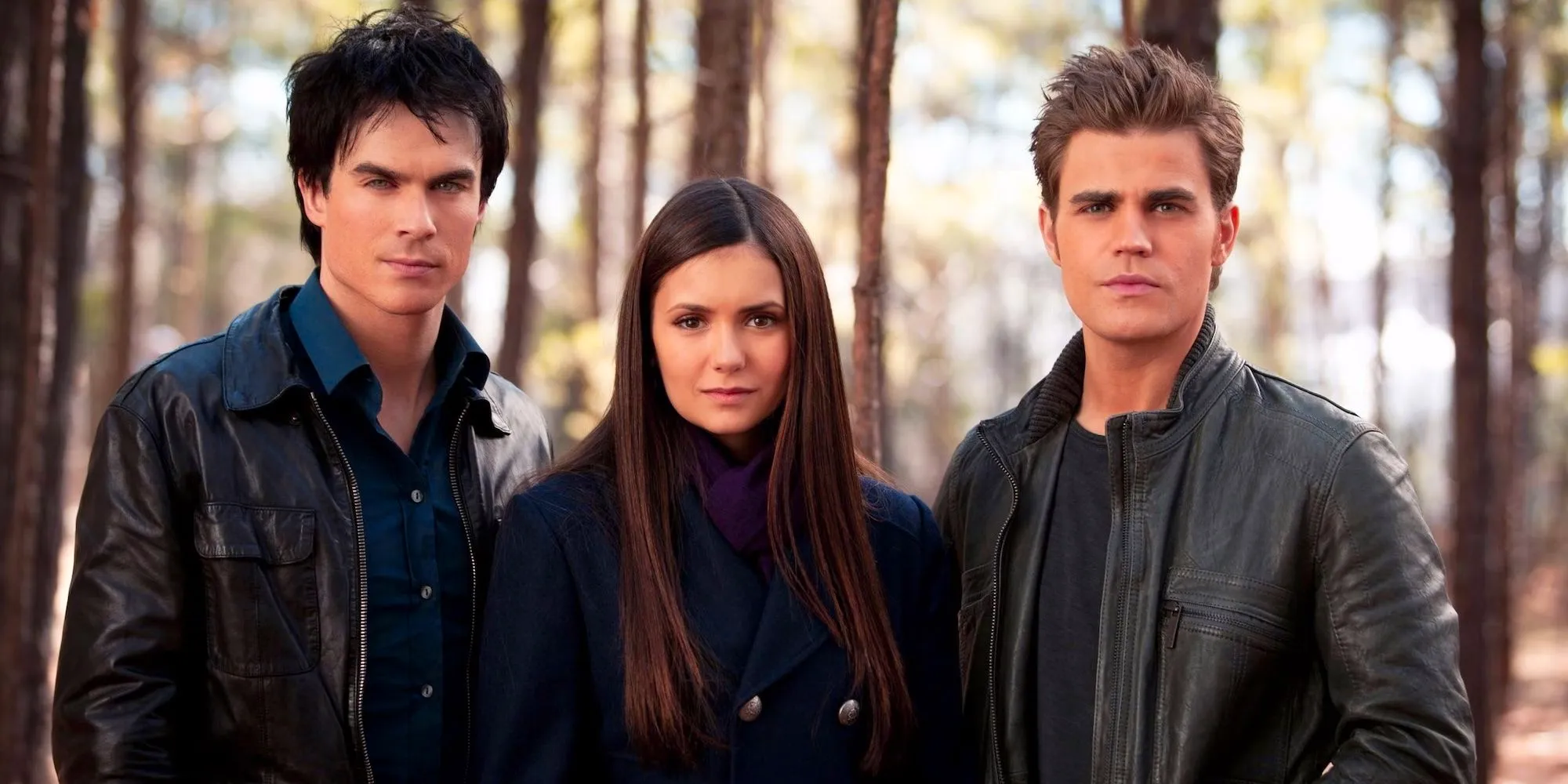 Stefan, Damon, and Elena in the woods staring at the camera in a promotional still in The Vampire Diaries Image