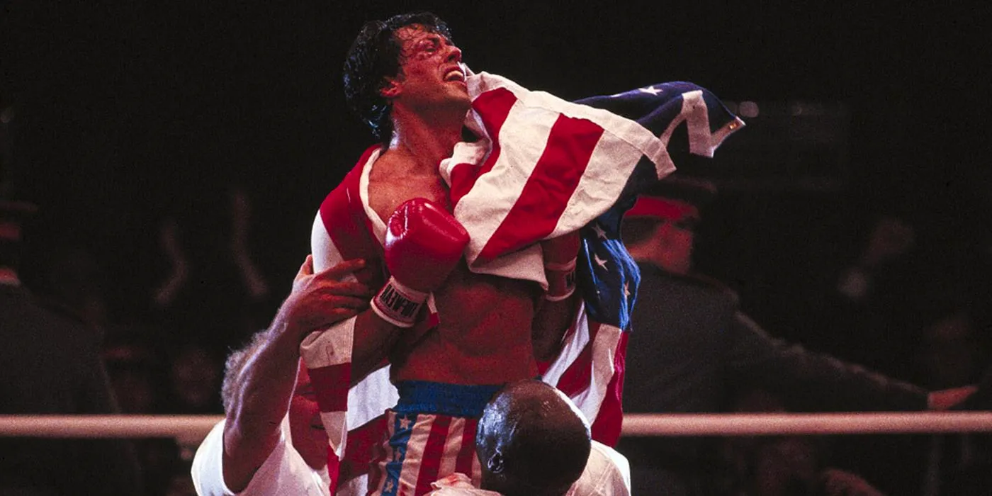 Sylvester Stallone being lifted in the air with an American flag wrapped around him in Rocky 4 Image