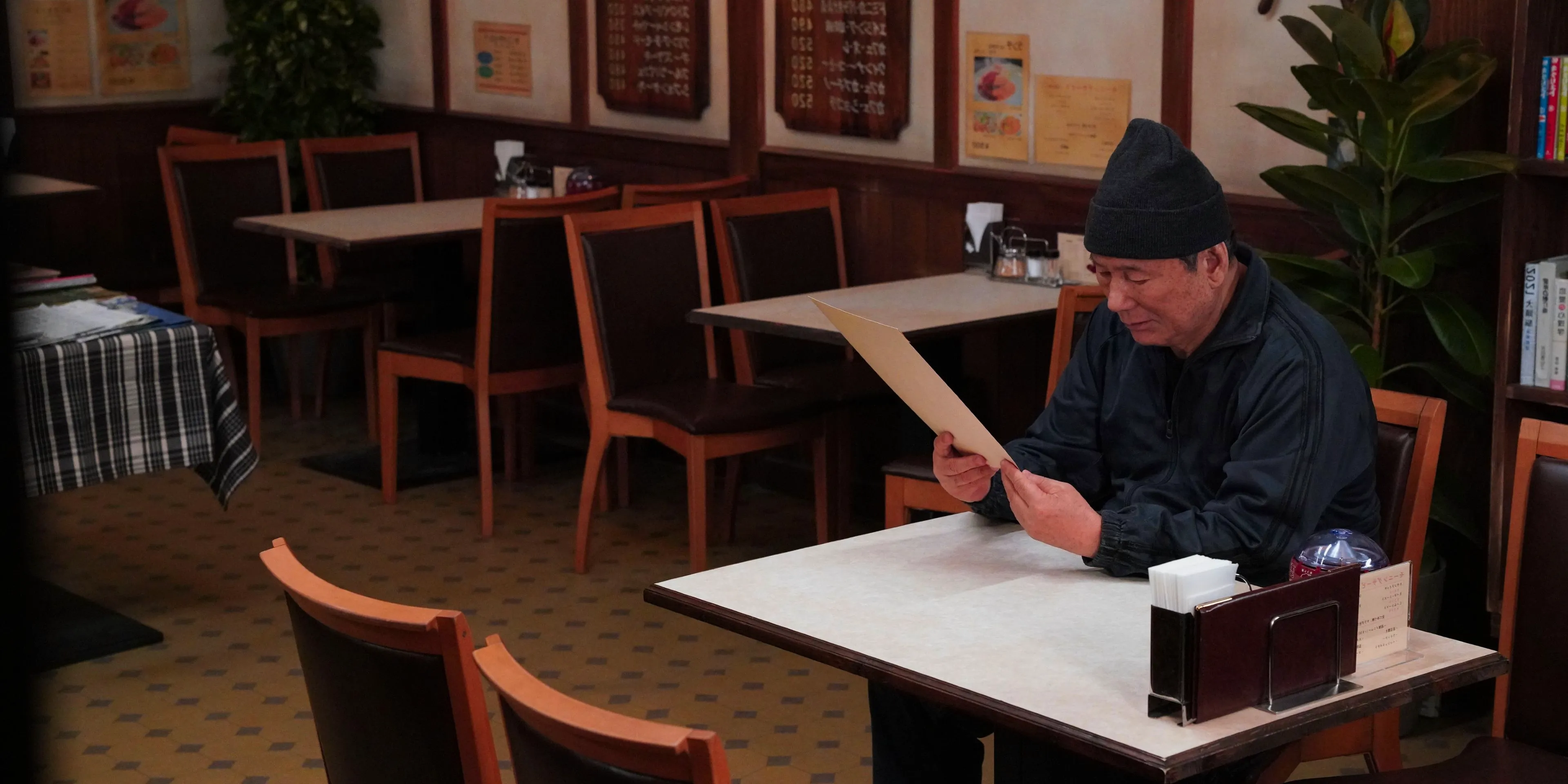 Takeshi Kitano seated at a cafe and studying an envelope left for him in Broken Rage Image