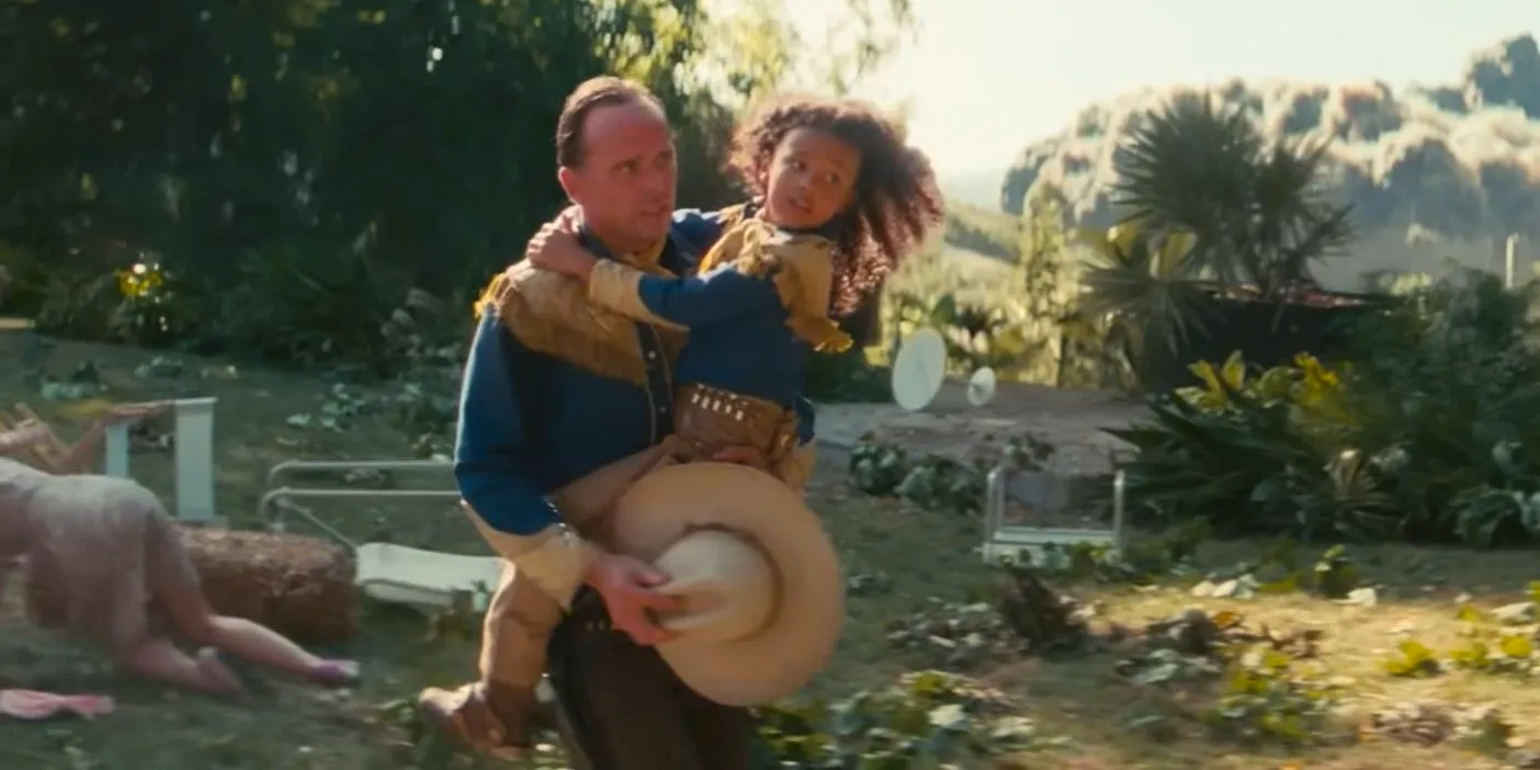 Teagan Meredith as Janey Howard being carried by Walton Goggins as Cooper Howard as the bombs fall in the Fallout show Image