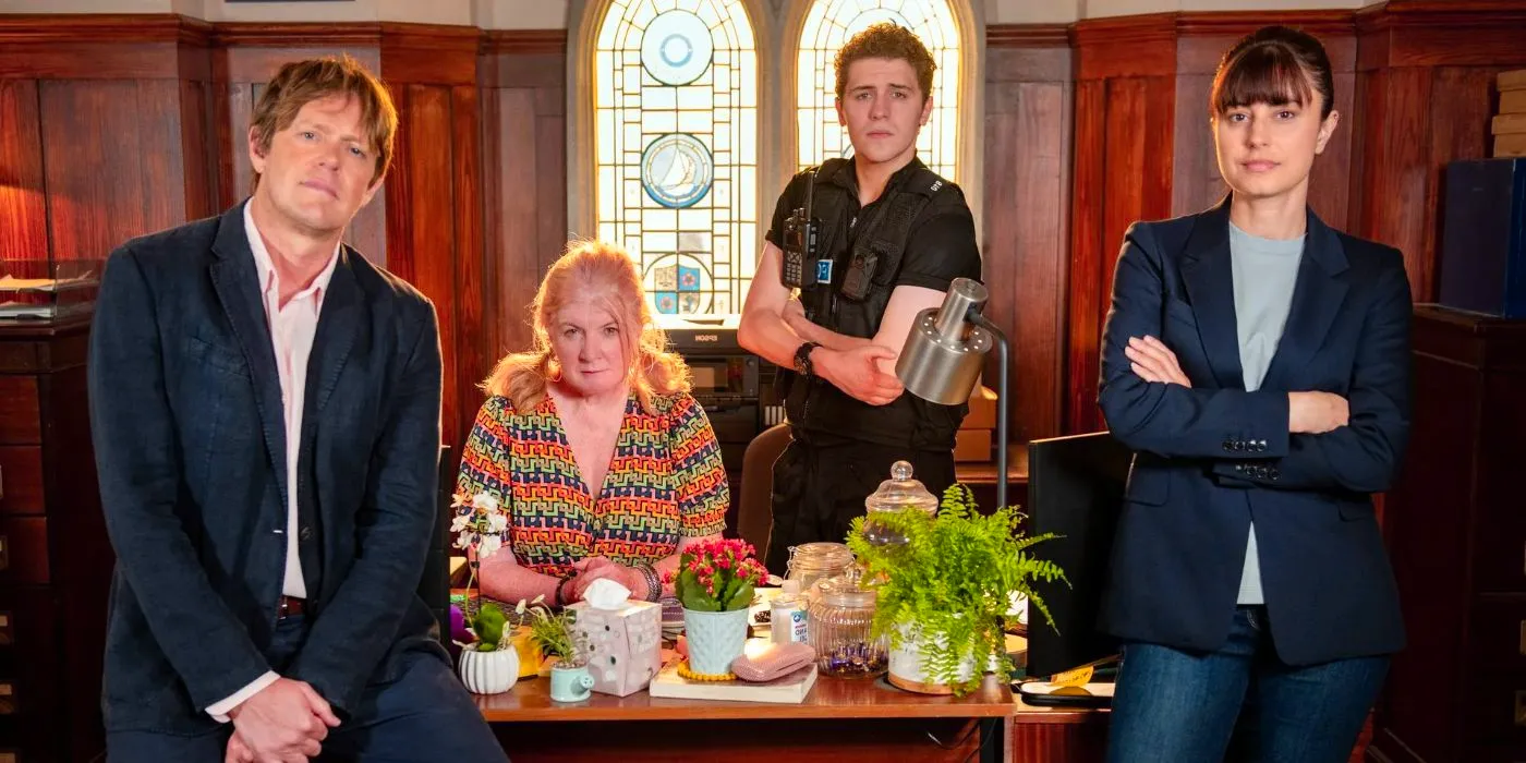 The cast of Beyond Paradise sitting on a desk in Beyond Paradise Image