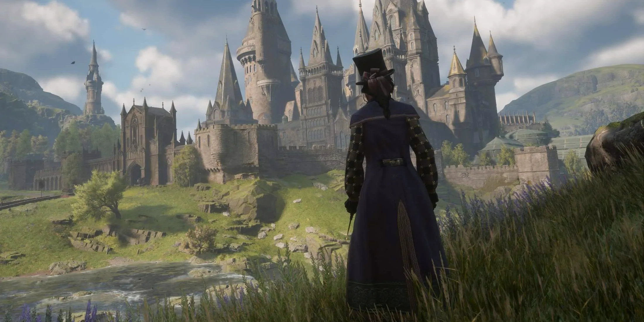 The player in Hogwarts Legacy wearing a coat and top hat stood outside of Hogwarts. Image