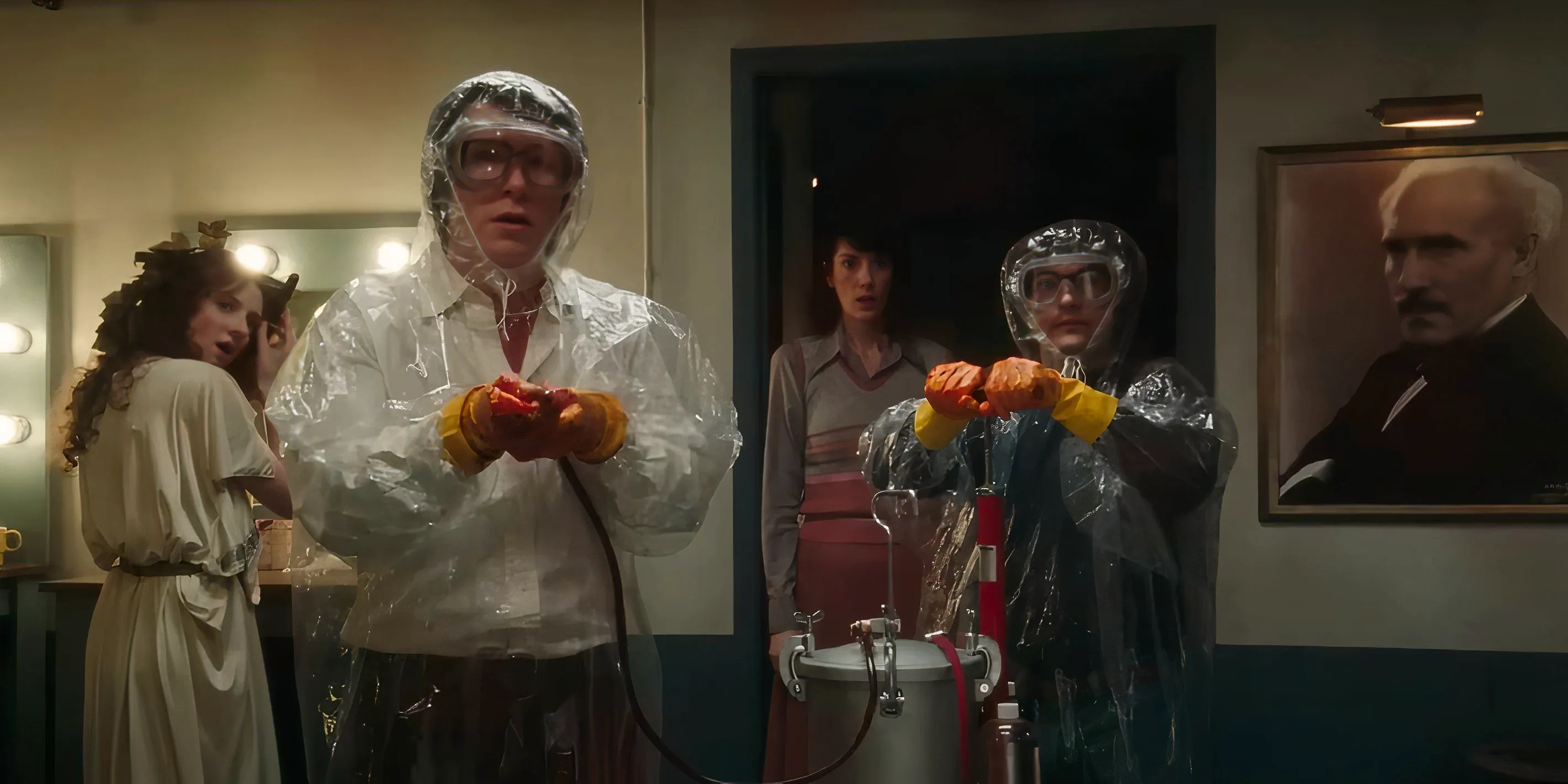 The SNL cast wears plastic suits near a pump in Saturday Night still Image