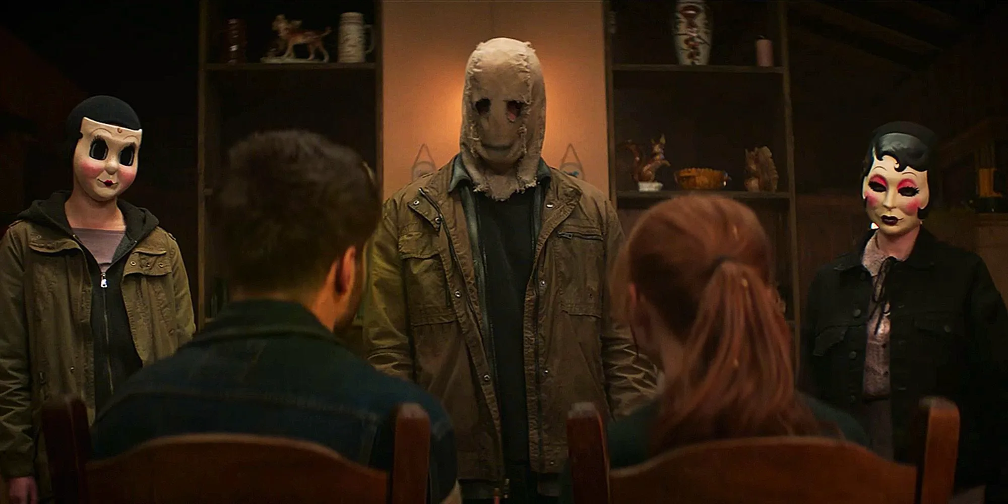 three masked people standing in front of a couple sitting down in The Strangers Chapter 1 Image