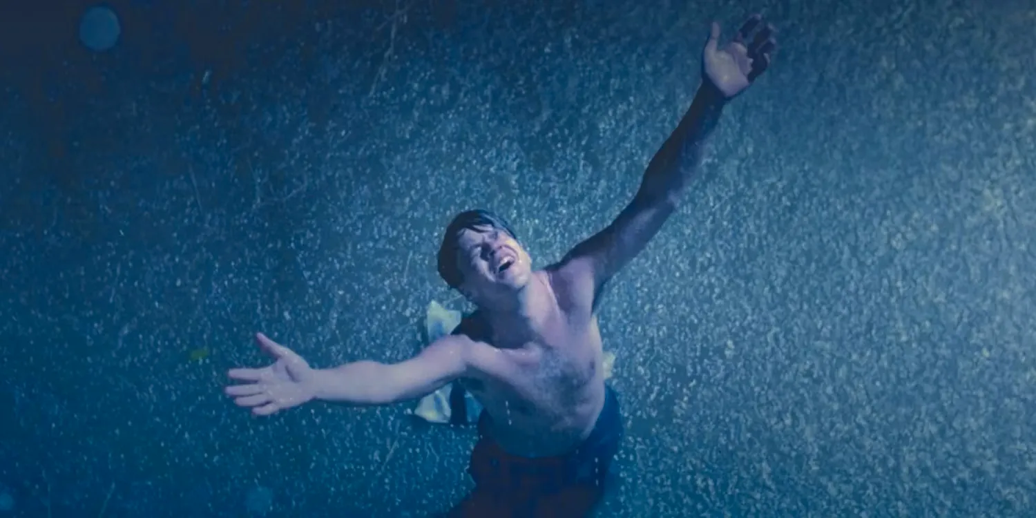 Tim Robbins as Andy Dufresne stands with his arms raised to the sky in the rain in The Shawshank Redemption. Image