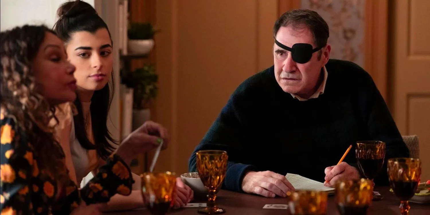 Vince Fish (Richard Kind) wearing an eyepatch and holding a pencil while sitting at a table with Inez (Daphne Rubin-Vega) and her daughter Ana (Lilian Rebelo) in Only Murders in the Building season 4, episode 2,  Image