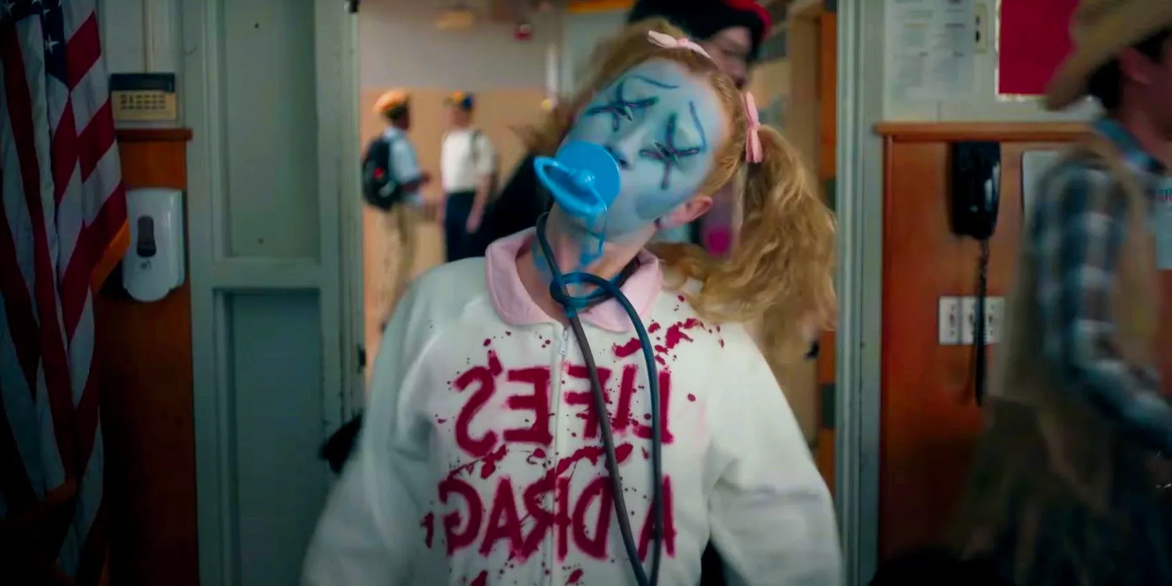 Women in pigtails and a pacifier in her mouth wearing a white hooding with Lifes A Drag written on it in blood in American Horror Stories season 3 trailer Image